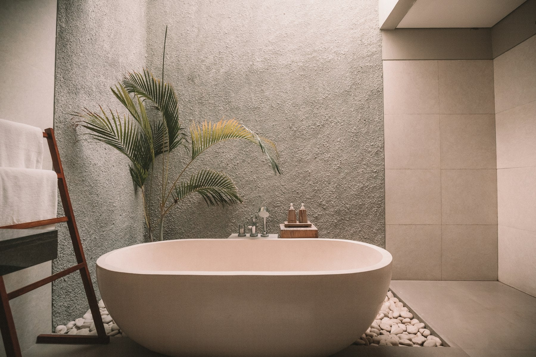 Luxury spa bathtub with natural skincare products, palm plant, and white stones